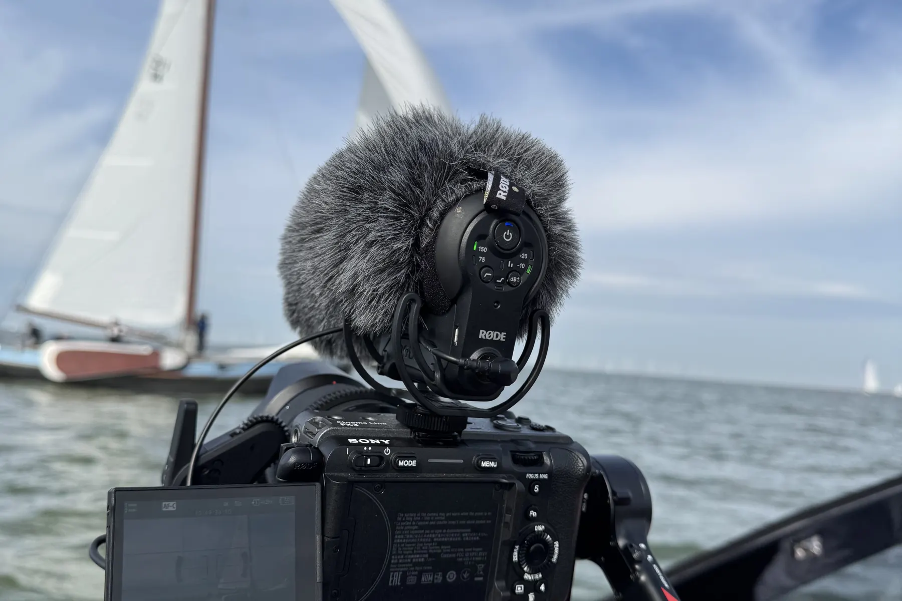 Camera met microfoon op een boot, met een skûtsje onder zeil op de achtergrond